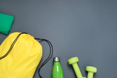 Photo of Yellow drawstring bag, thermo bottle and dumbbells on grey background, flat lay. Space for text