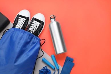 Photo of Blue drawstring bag, thermo bottle, skipping rope and sneakers on red background, flat lay. Space for text