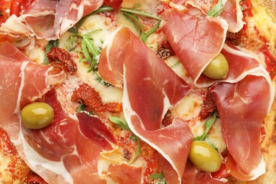 Photo of Tasty pizza with cured ham, olives and sun-dried tomato as background, top view