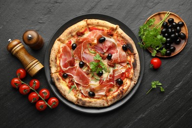 Photo of Tasty pizza with cured ham, olives, tomatoes and parsley on black table, top view