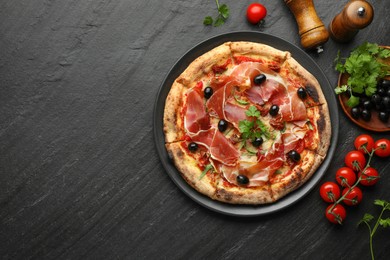 Photo of Tasty pizza with cured ham, olives, tomatoes and parsley on black table, top view. Space for text