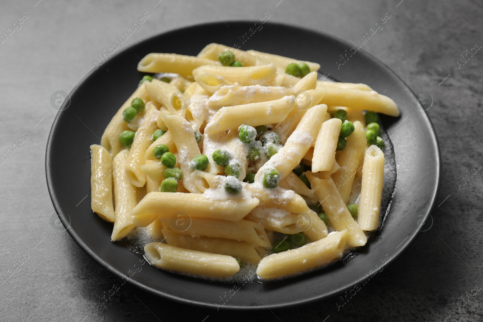 Photo of Delicious pasta with green peas and creamy sauce on grey table