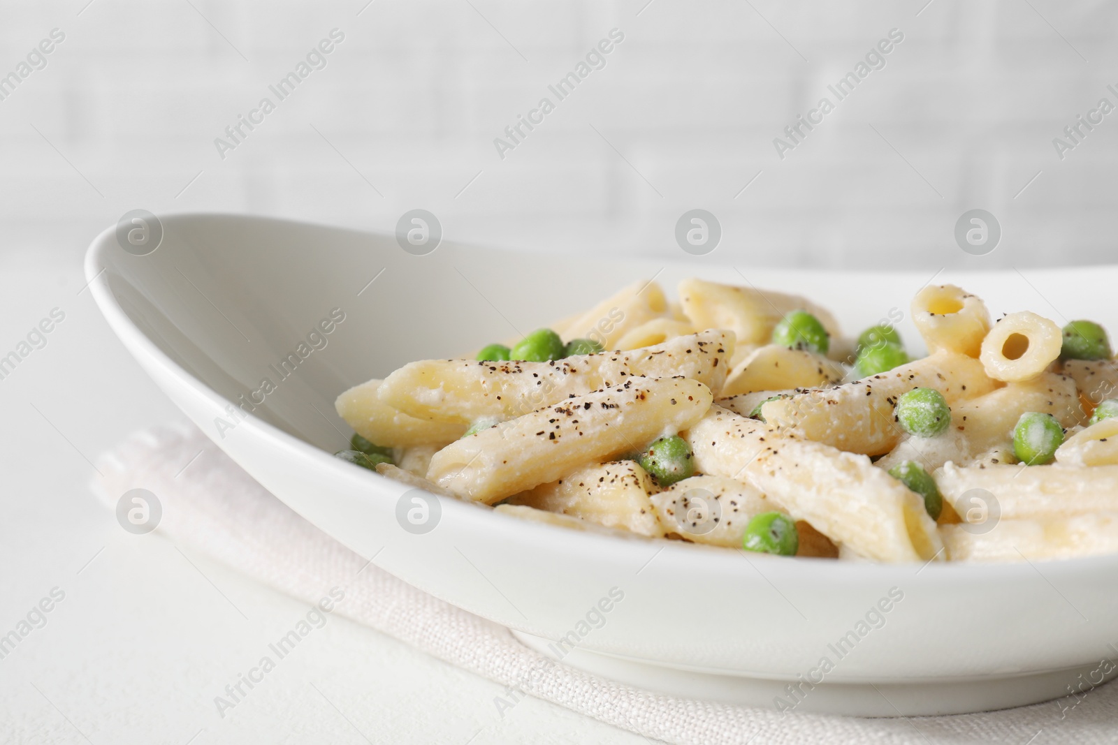 Photo of Delicious pasta with green peas and creamy sauce in bowl on white table, closeup