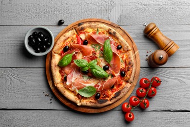 Photo of Tasty pizza with cured ham, olives, tomatoes and basil on gray wooden table, flat lay