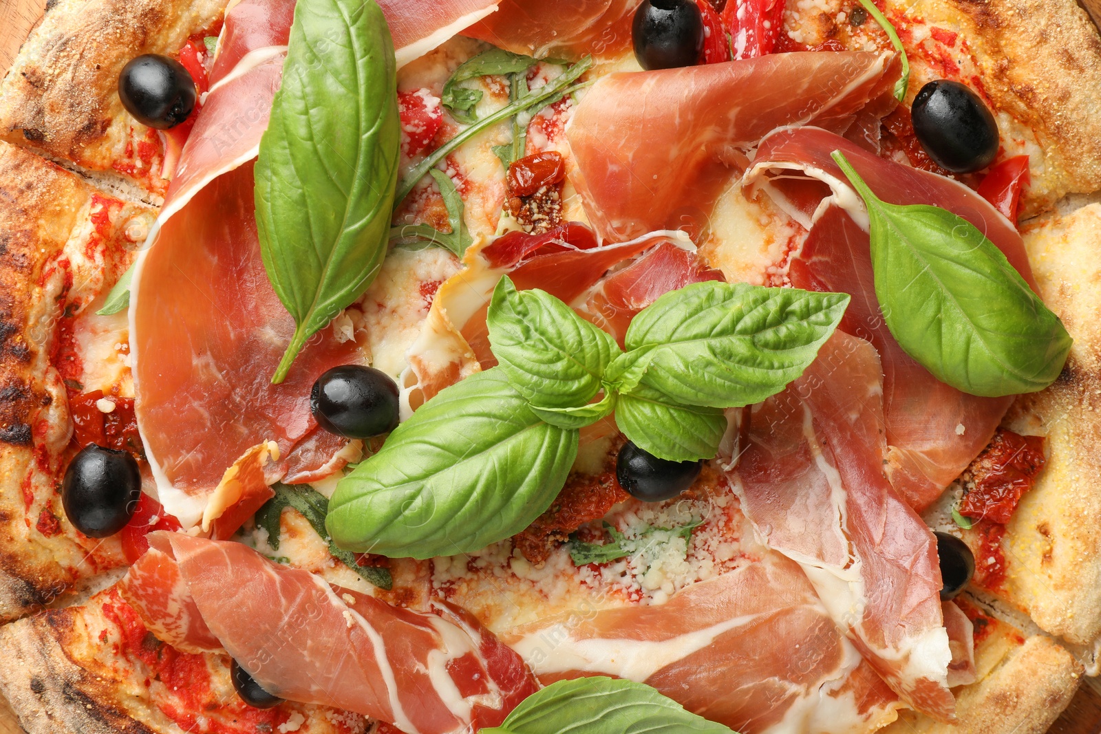 Photo of Tasty pizza with cured ham, olives, sun-dried tomato and basil as background, top view