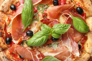 Photo of Tasty pizza with cured ham, olives, sun-dried tomato and basil as background, top view