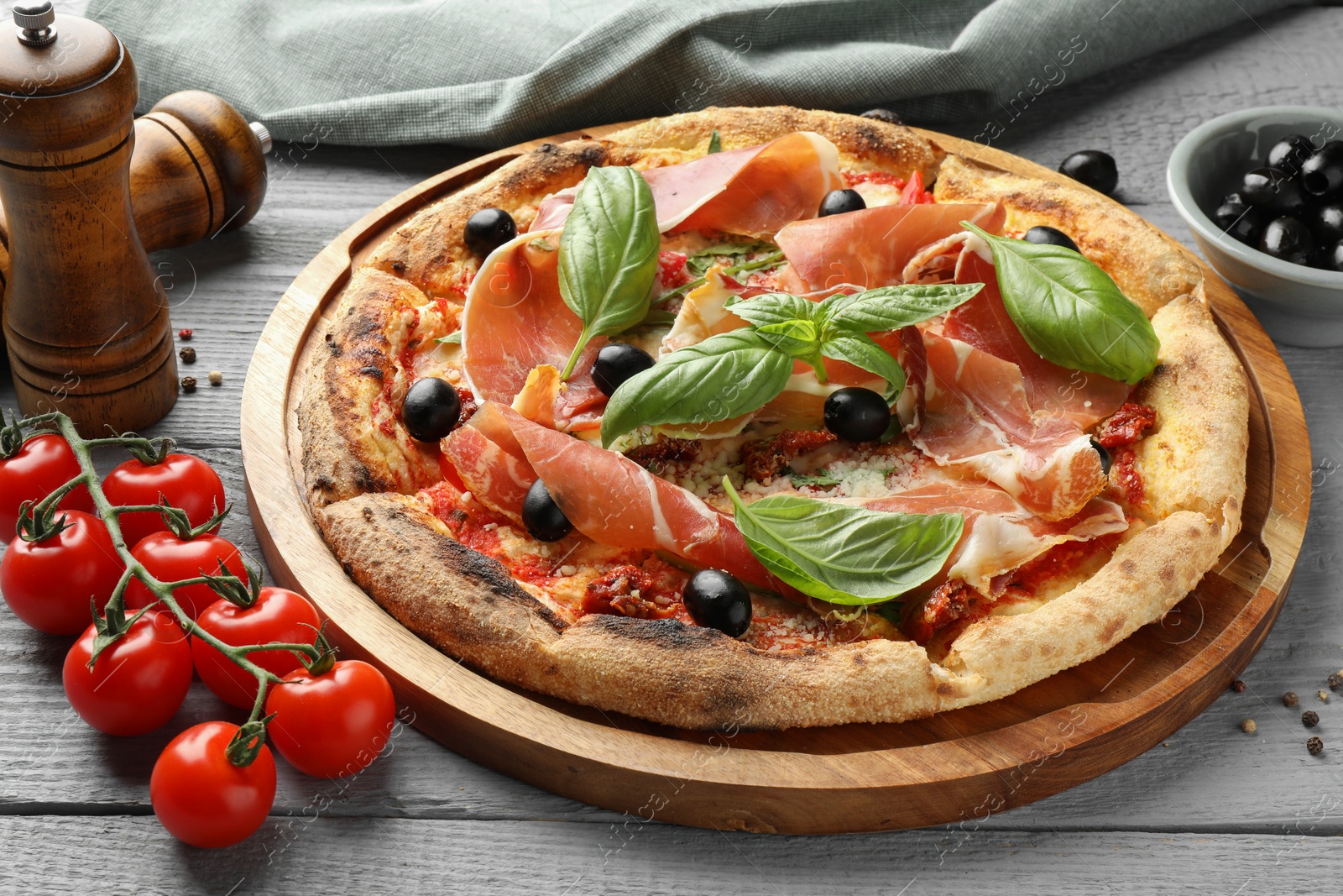 Photo of Tasty pizza with cured ham, olives, tomatoes and basil on gray wooden table, closeup