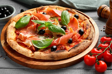 Tasty pizza with cured ham, olives, tomatoes and basil on gray wooden table, closeup