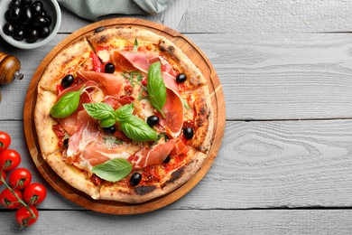 Tasty pizza with cured ham, olives, tomatoes and basil on gray wooden table, flat lay. Space for text