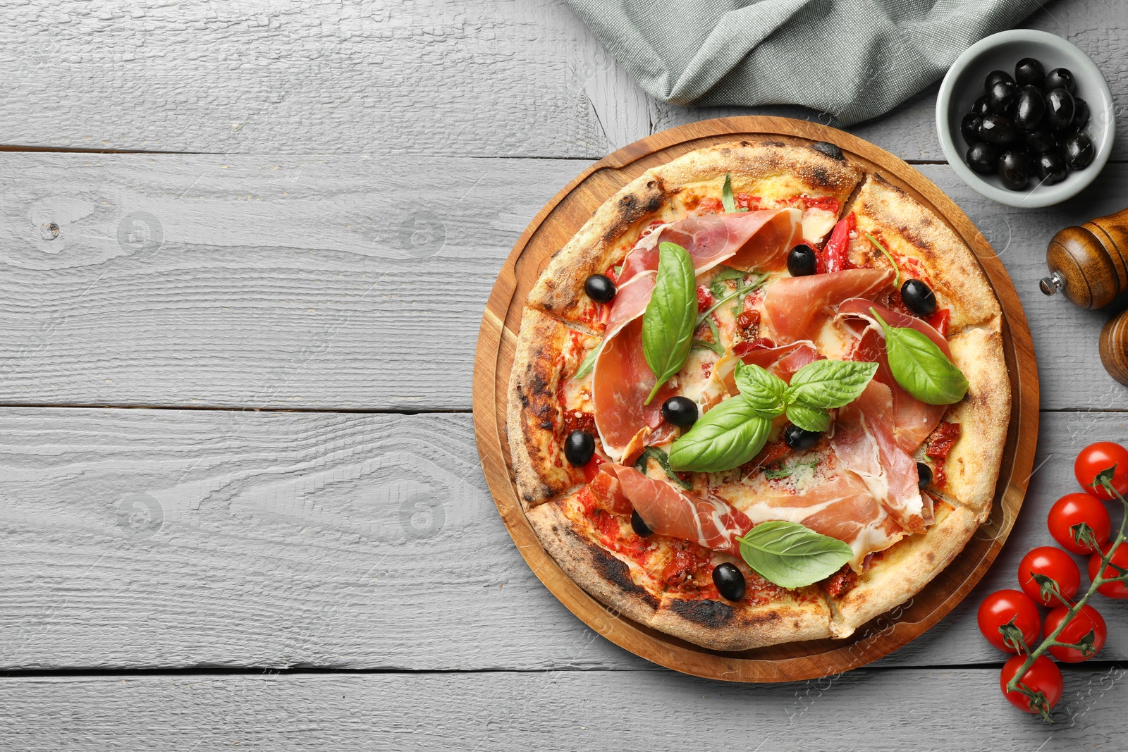 Photo of Tasty pizza with cured ham, olives, tomatoes and basil on gray wooden table, flat lay. Space for text