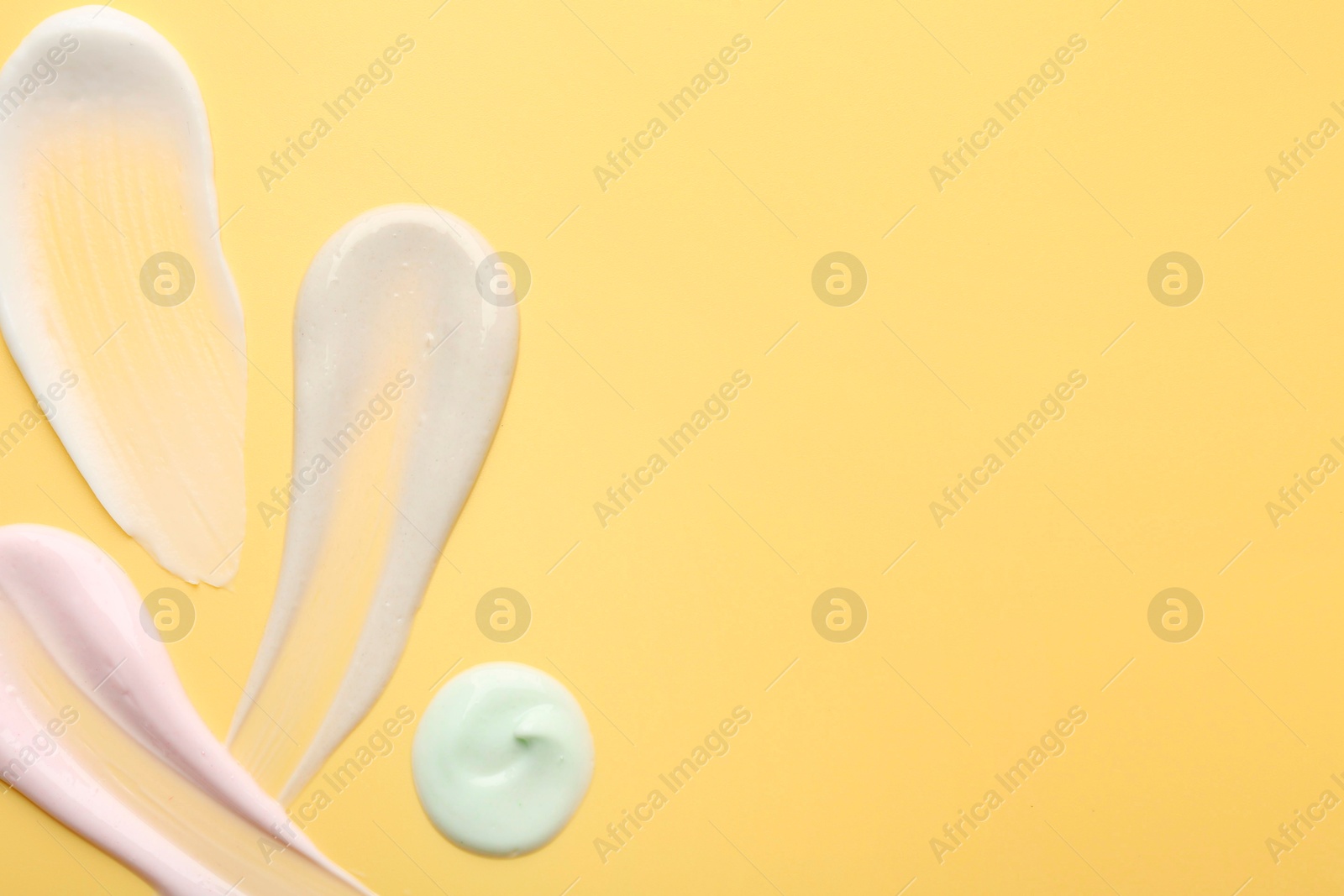 Photo of Samples of face cream on yellow background, top view. Space for text