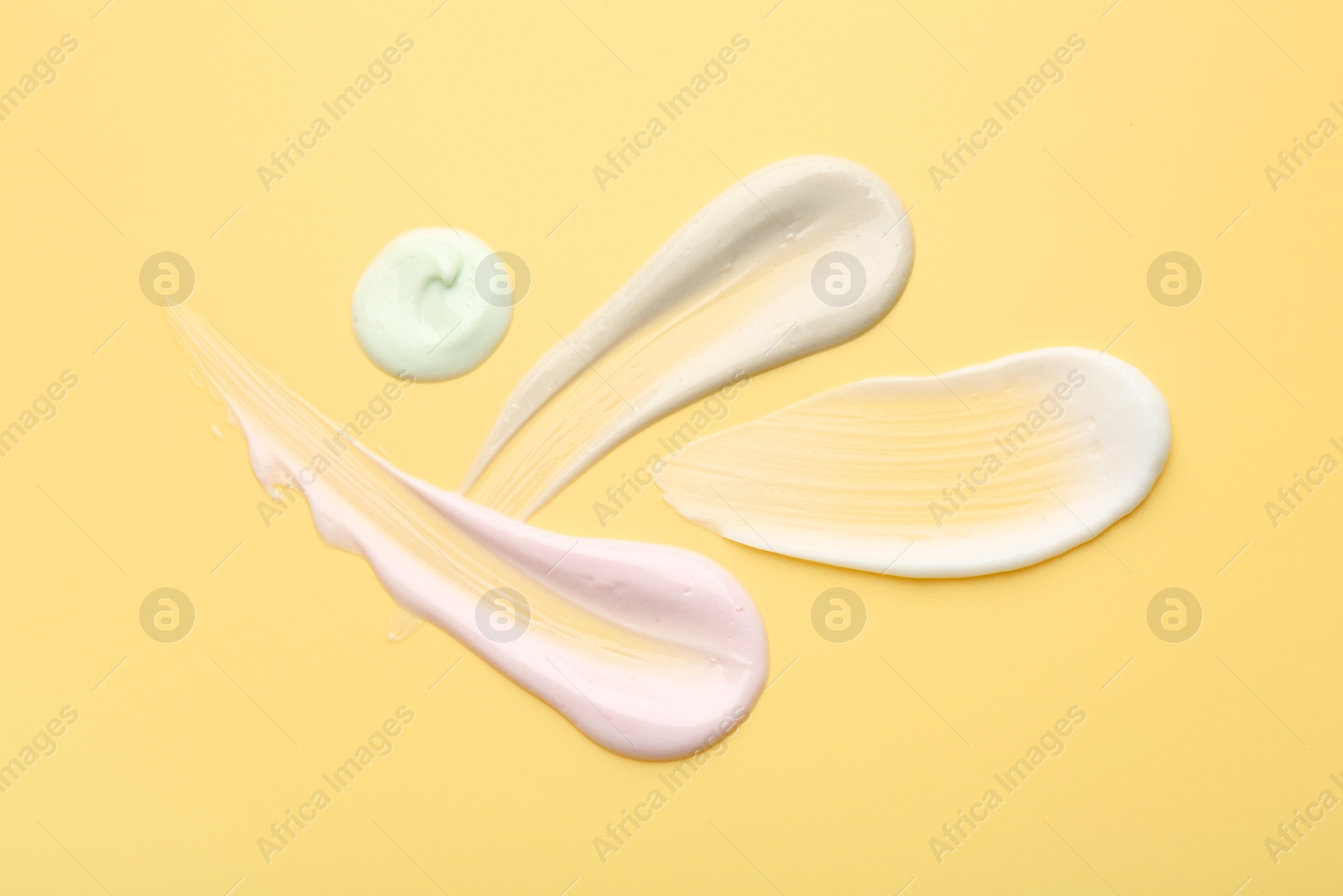 Photo of Samples of face cream on yellow background, top view