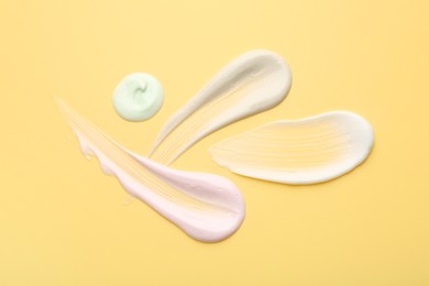 Photo of Samples of face cream on yellow background, top view