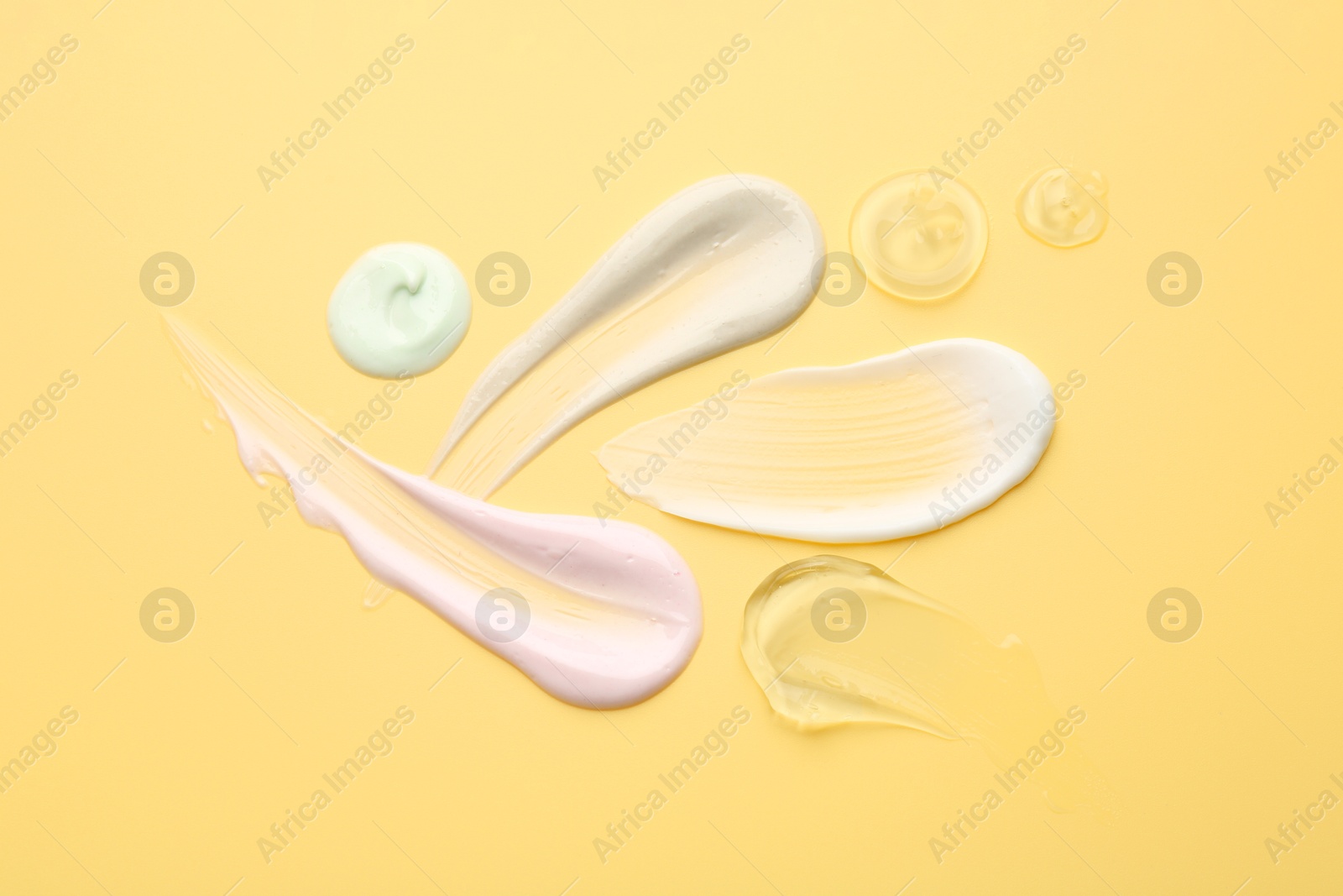 Photo of Samples of face cream on yellow background, top view