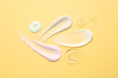 Photo of Samples of face cream on yellow background, top view