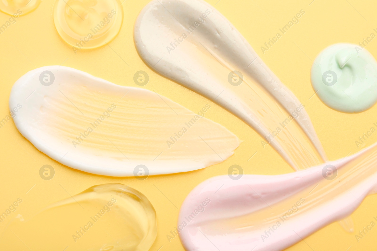 Photo of Samples of face cream on yellow background, top view