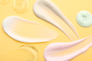 Photo of Samples of face cream on yellow background, top view