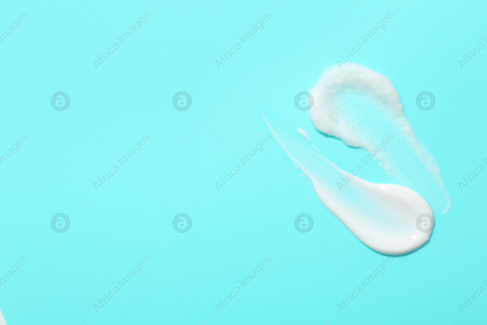 Photo of Samples of face cream on light blue background, top view. Space for text