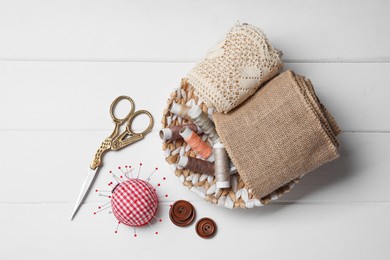 Photo of Checkered pincushion with pins and other sewing tools on white wooden table, flat lay