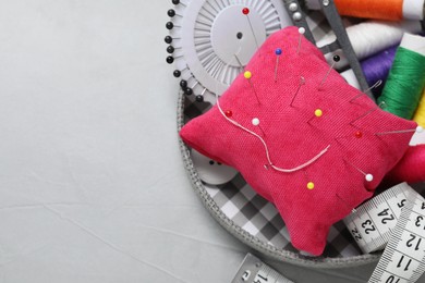 Photo of Red pincushion with pins and other sewing tools on grey table, closeup. Space for text