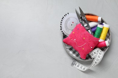 Photo of Red pincushion with pins and other sewing tools on grey table, flat lay. Space for text