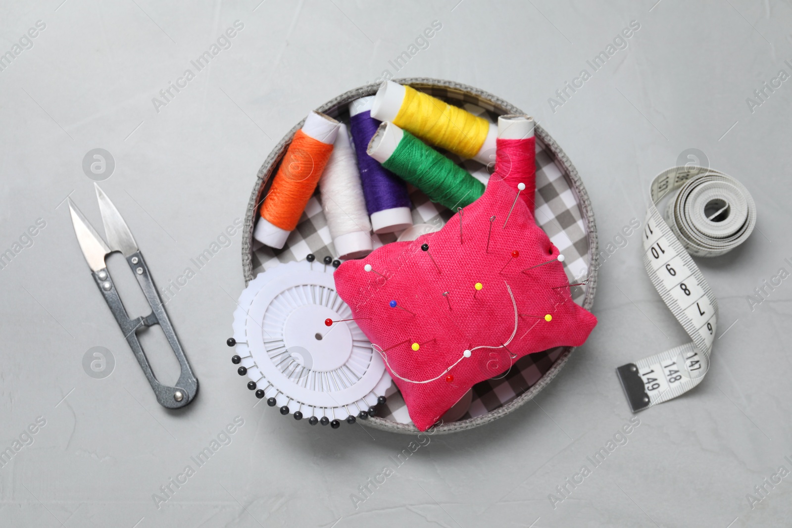 Photo of Red pincushion with pins and other sewing tools on grey table, flat lay