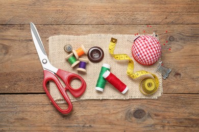 Photo of Checkered pincushion with pins and other sewing tools on wooden table, flat lay