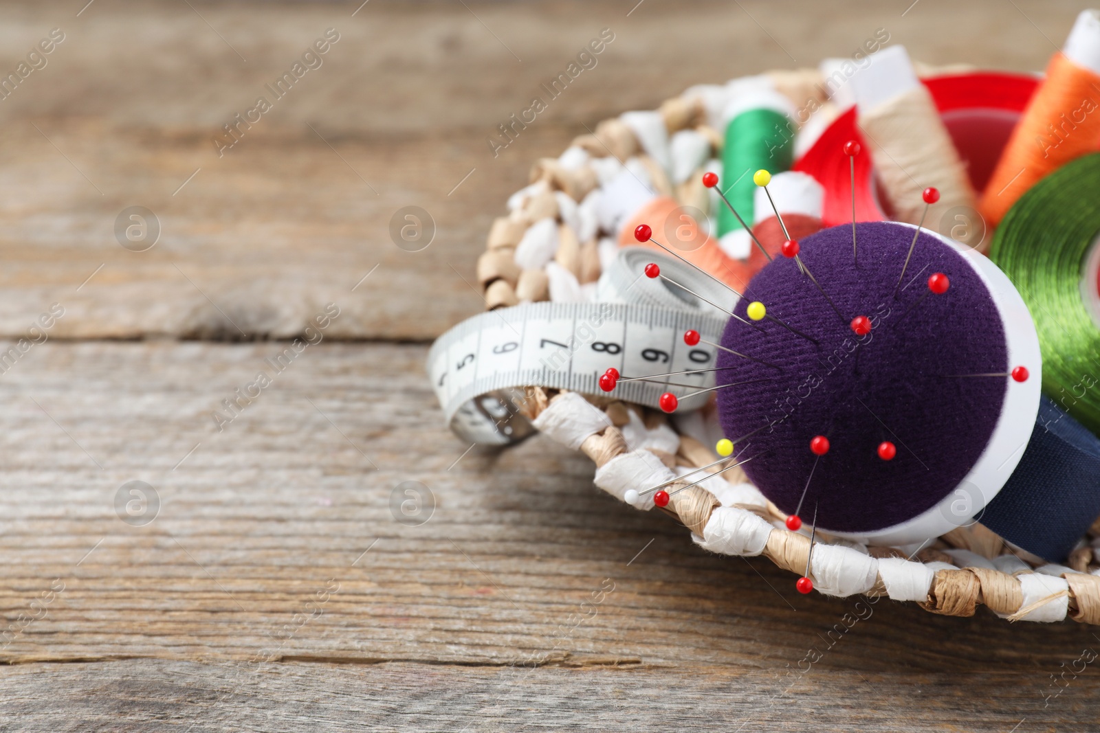 Photo of Blue pincushion with pins and other sewing tools on wooden table. Space for text