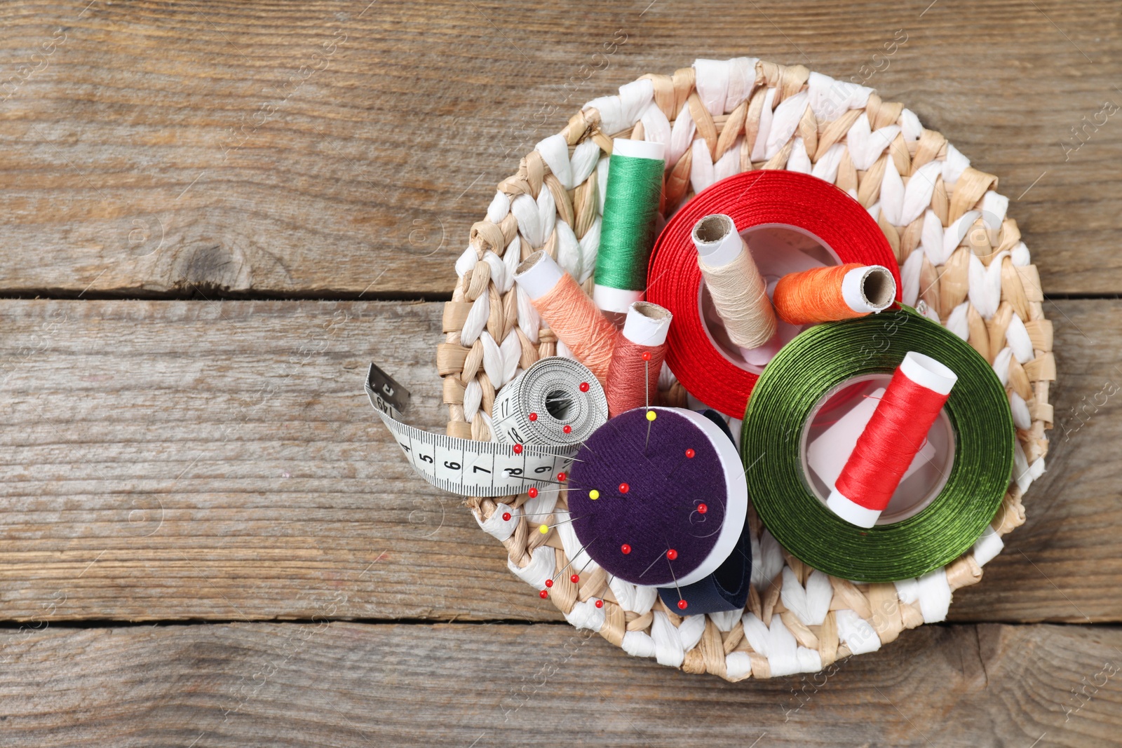 Photo of Blue pincushion with pins and other sewing tools on wooden table, top view. Space for text