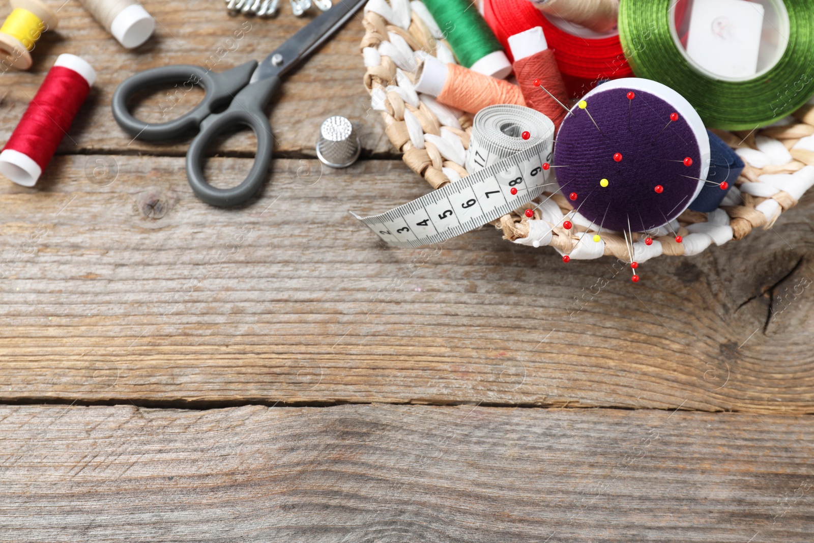 Photo of Blue pincushion with pins and other sewing tools on wooden table, flat lay. Space for text