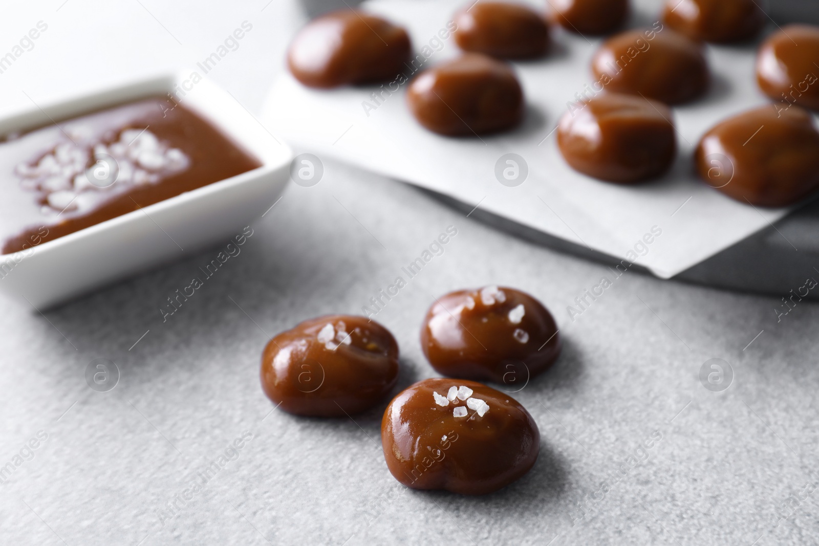 Photo of Tasty candies, caramel sauce and salt on light grey table