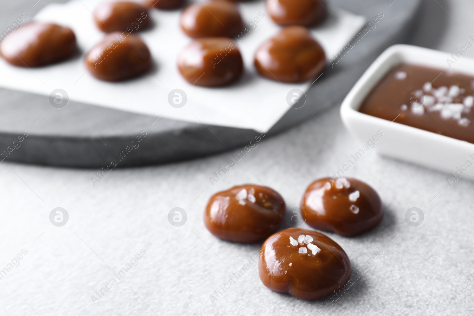 Photo of Tasty candies, caramel sauce and salt on light grey table