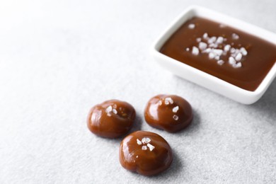 Photo of Tasty candies, caramel sauce and salt on light grey table, space for text