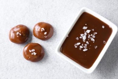 Photo of Tasty candies, caramel sauce and salt on light grey table, top view
