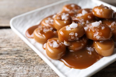 Photo of Tasty candies, caramel sauce and salt on wooden table, closeup