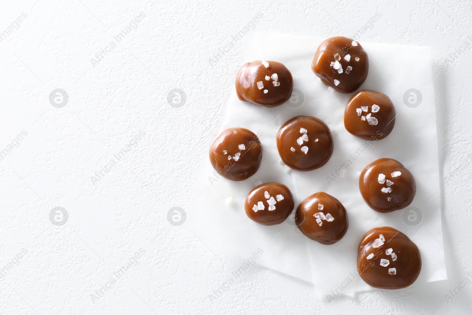 Photo of Tasty caramel candies and salt on white table, top view. Space for text