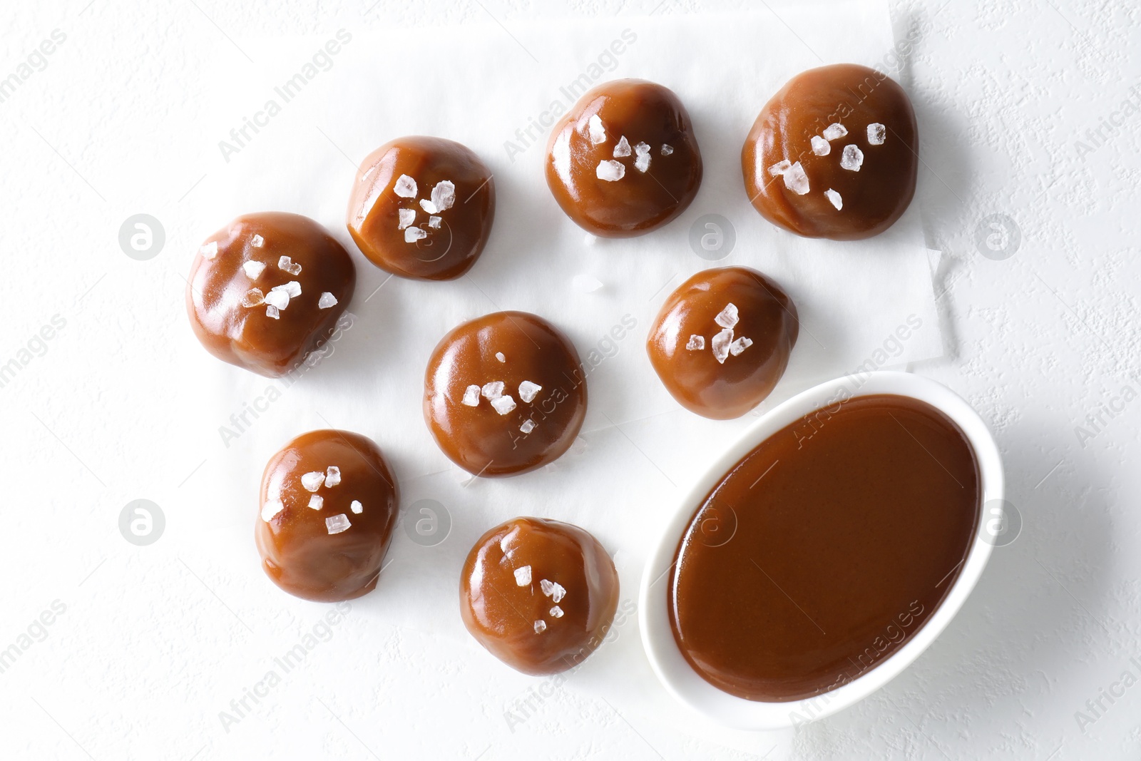 Photo of Tasty candies, caramel sauce and salt on white table, top view