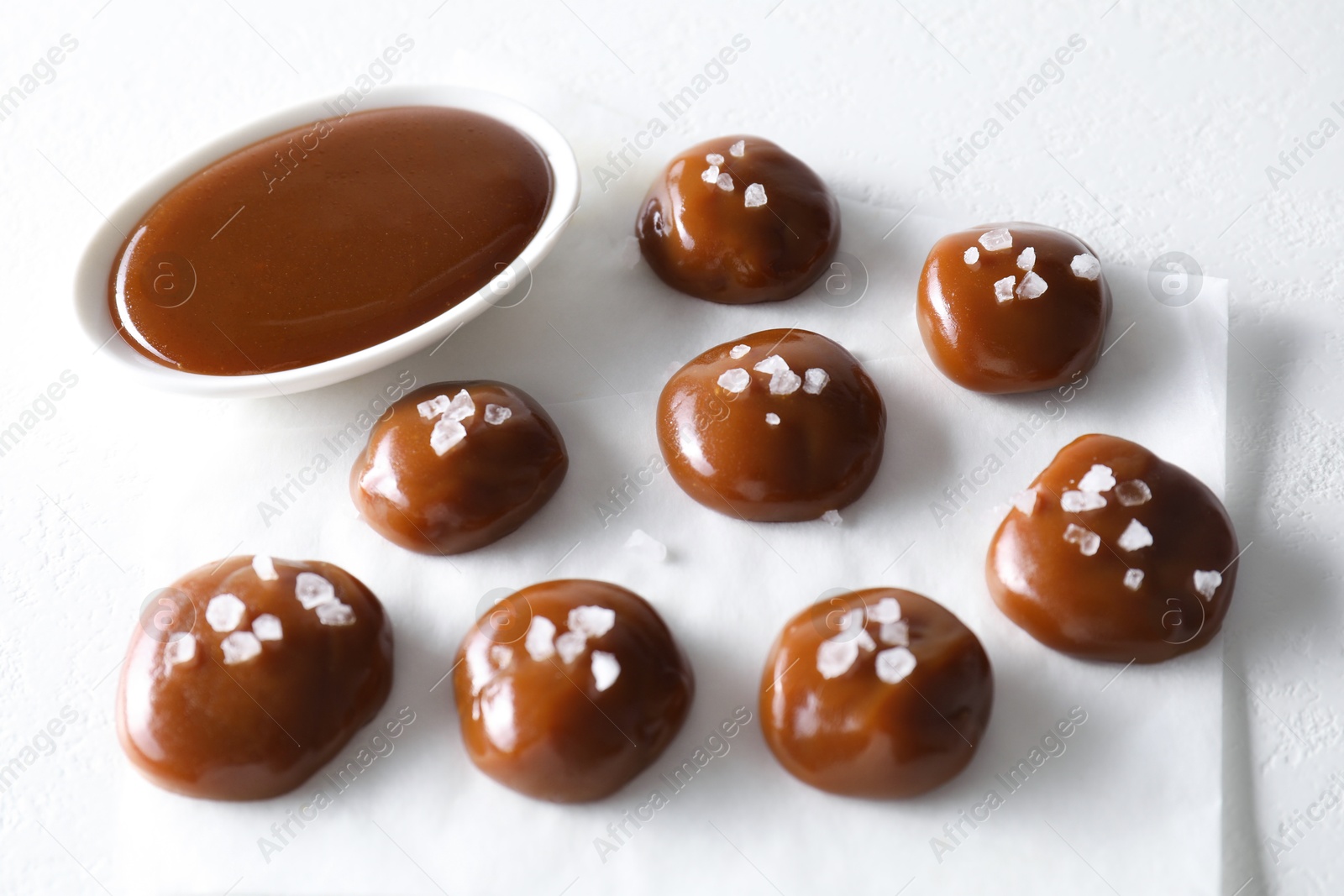 Photo of Tasty candies, caramel sauce and salt on white table