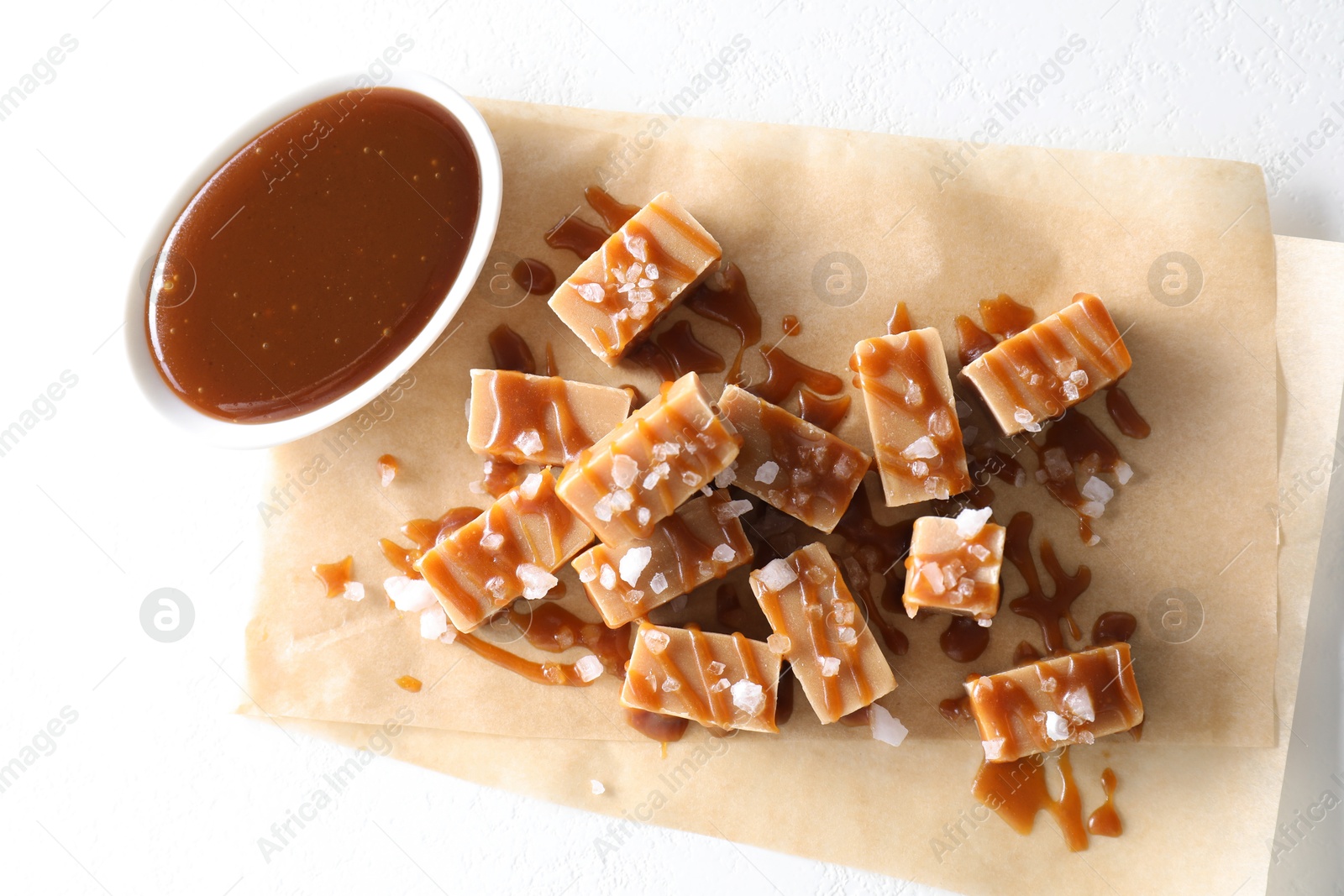 Photo of Tasty candies, caramel sauce and salt on white table, top view