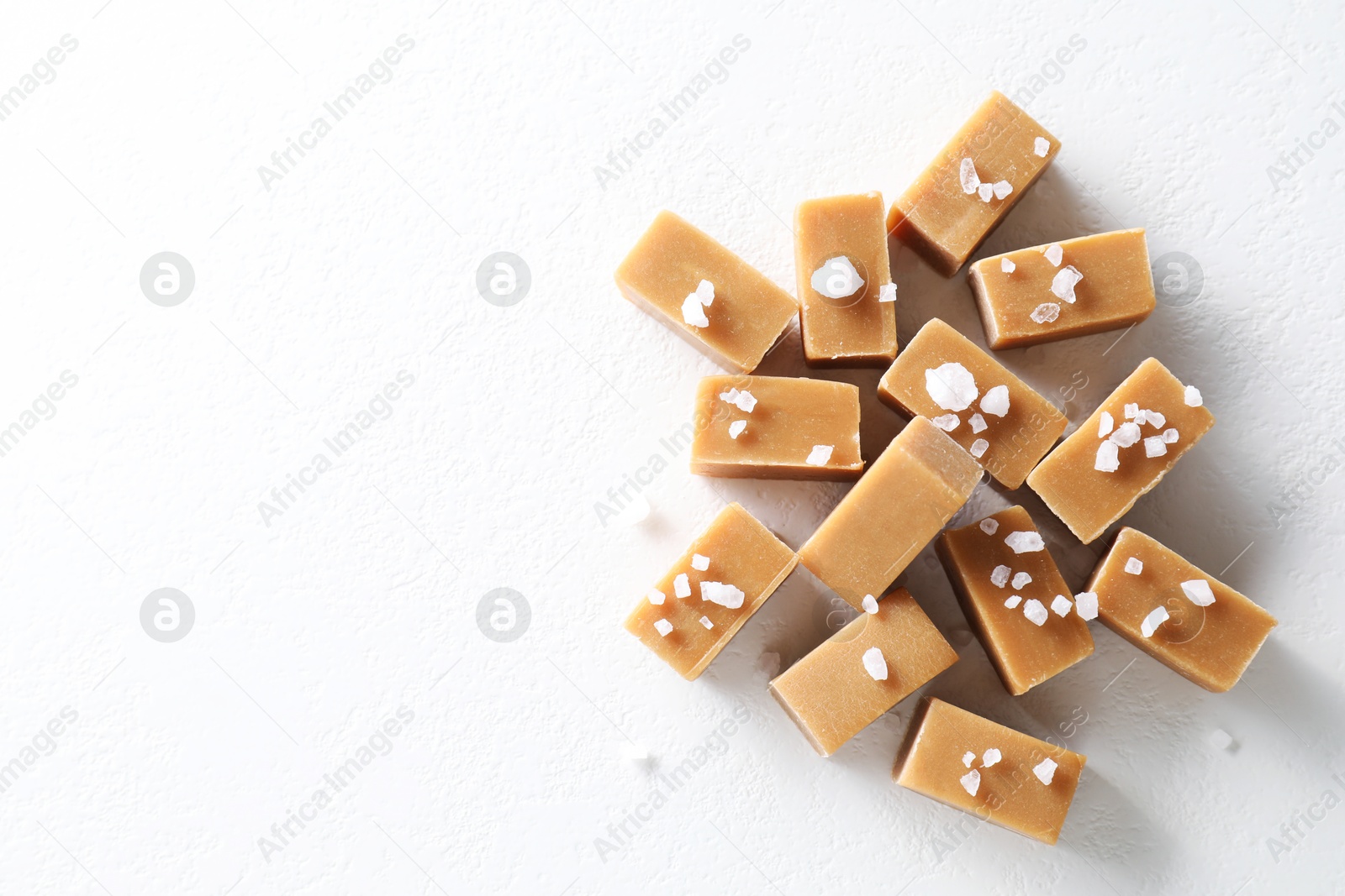 Photo of Tasty caramel candies and salt on white table, top view. Space for text