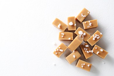 Photo of Tasty caramel candies and salt on white table, top view. Space for text