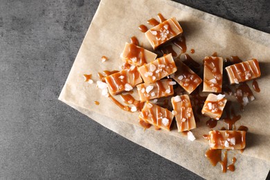 Photo of Tasty candies, caramel sauce and salt on grey table, top view. Space for text