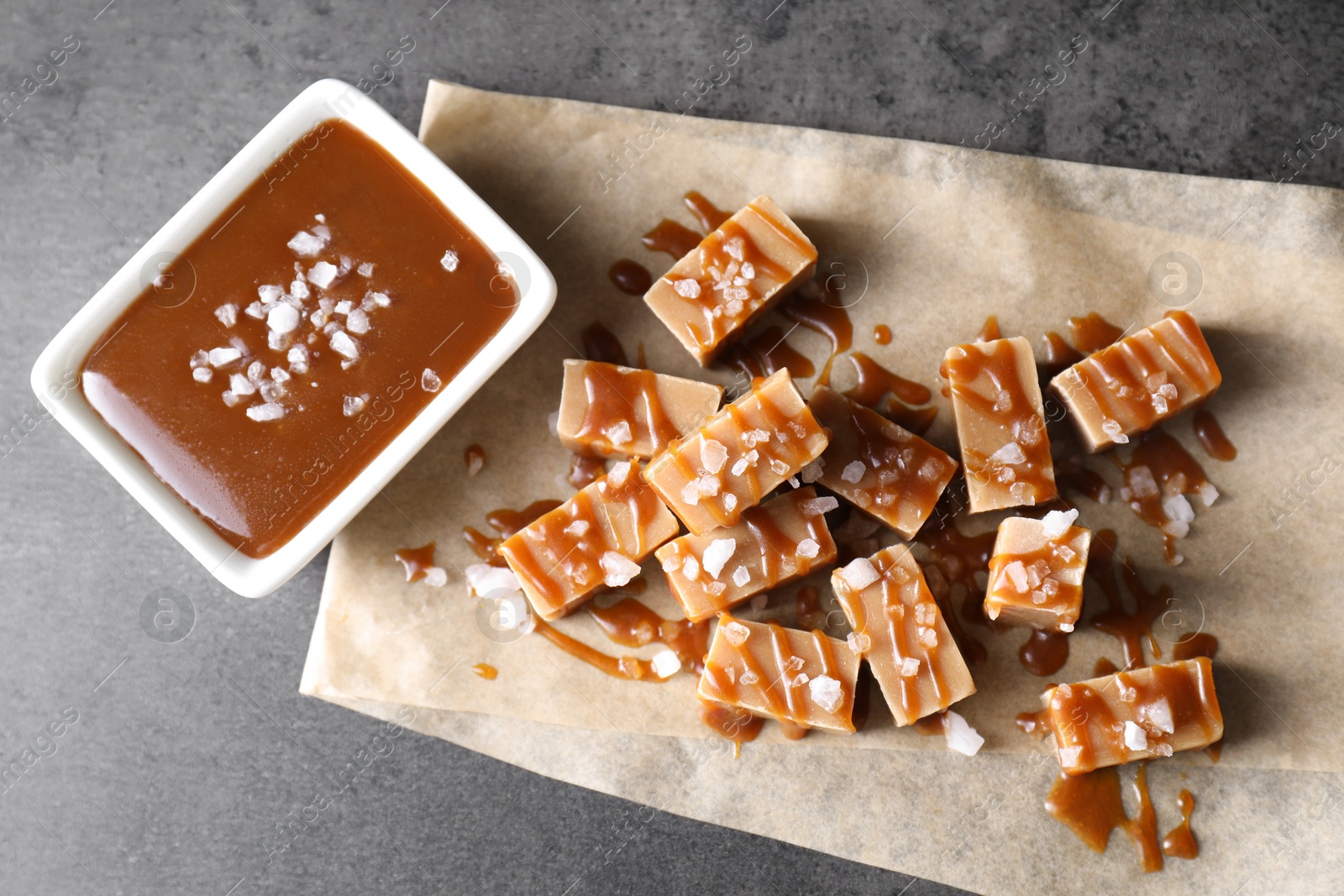 Photo of Tasty candies, caramel sauce and salt on grey table, top view