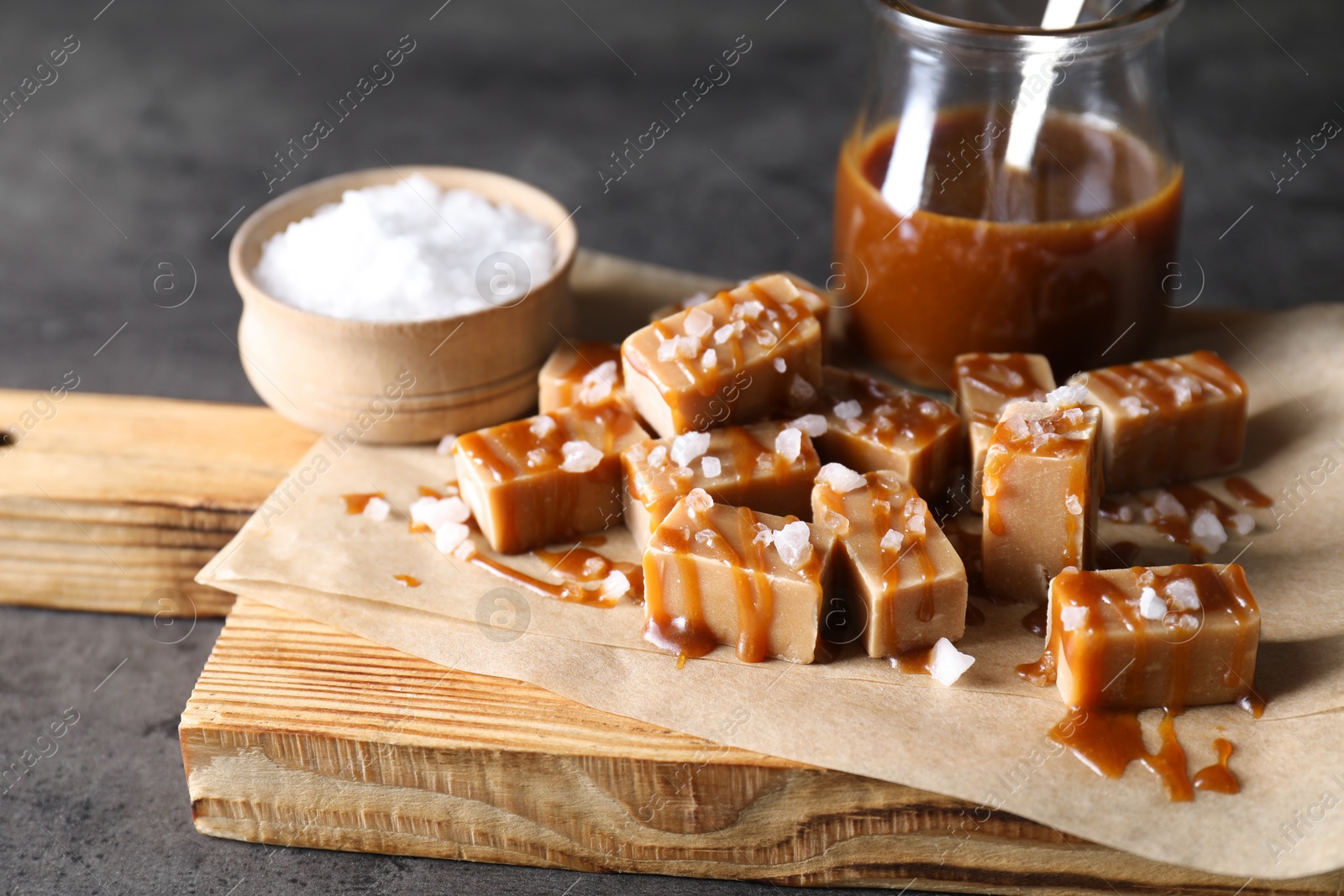 Photo of Tasty candies, caramel sauce and salt on grey table, closeup