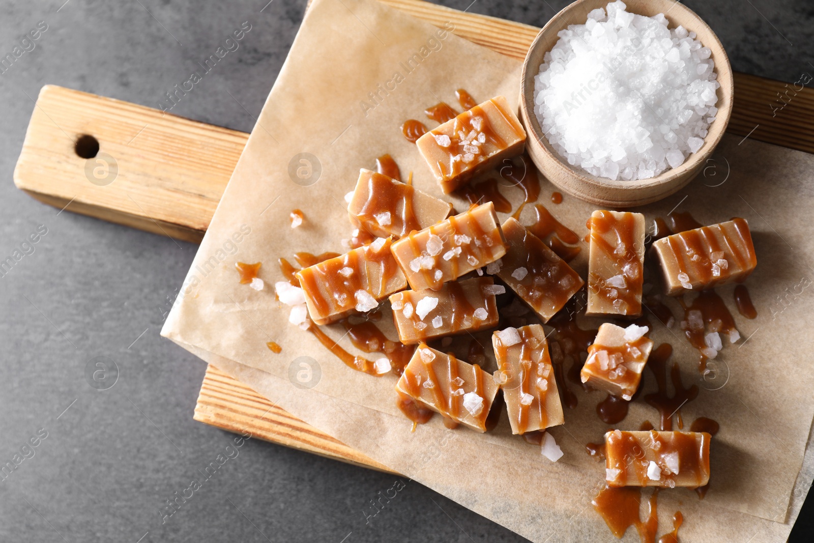 Photo of Tasty candies, caramel sauce and salt on grey table, top view