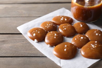 Photo of Tasty candies, caramel sauce and salt on wooden table, closeup