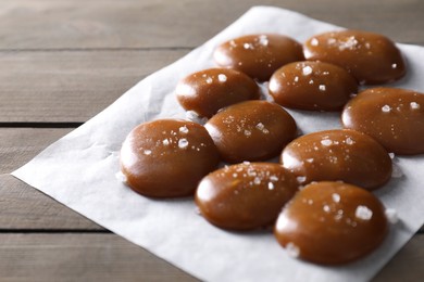 Photo of Tasty caramel candies and salt on wooden table, closeup