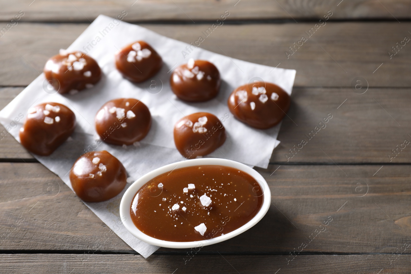 Photo of Tasty candies, caramel sauce and salt on wooden table