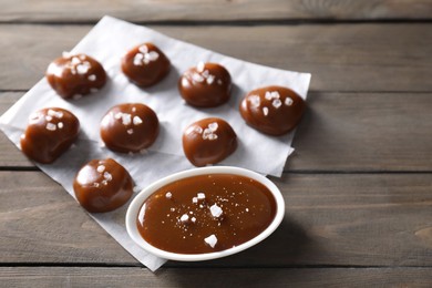 Photo of Tasty candies, caramel sauce and salt on wooden table