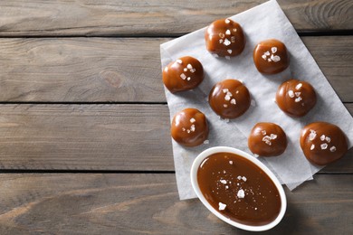 Photo of Tasty candies, caramel sauce and salt on wooden table, top view. Space for text